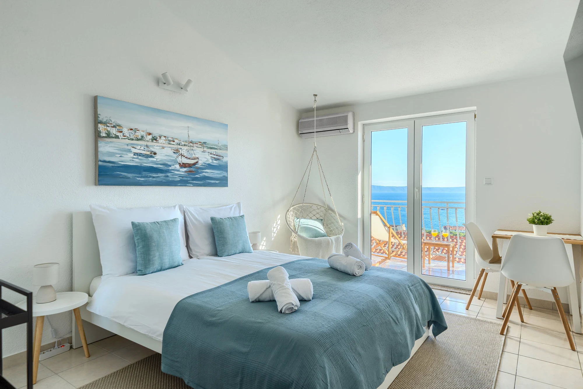Sea View Studio One with blue bedding, woven hanging chair and sea-facing balcony